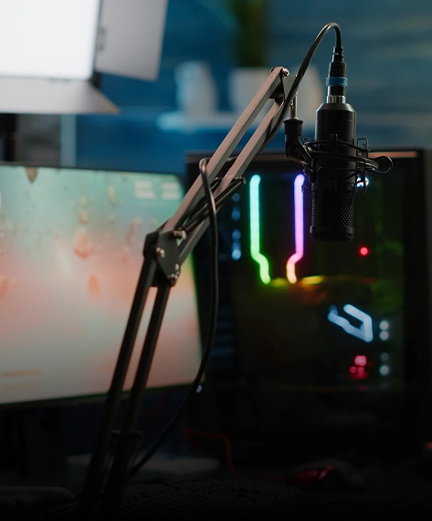 Een moderne gaming- en streamingopstelling met twee monitoren, een microfoon op een verstelbare standaard en een verlichte pc-toren. De sfeer is goed verlicht en gericht op technologie