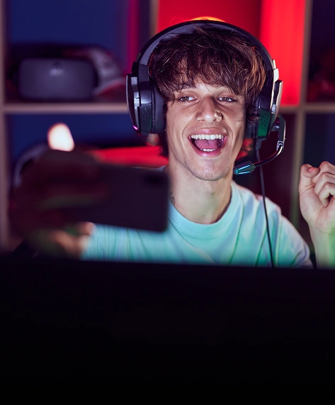 Lachende persoon met koptelefoon en microfoon, livestreamend met een smartphone. Kleurrijke neonlichten op de achtergrond zorgen voor een levendige, energieke sfeer